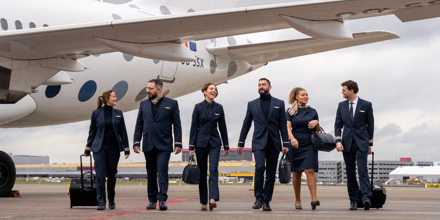 Cabin crew in formal attire next to an airplane.