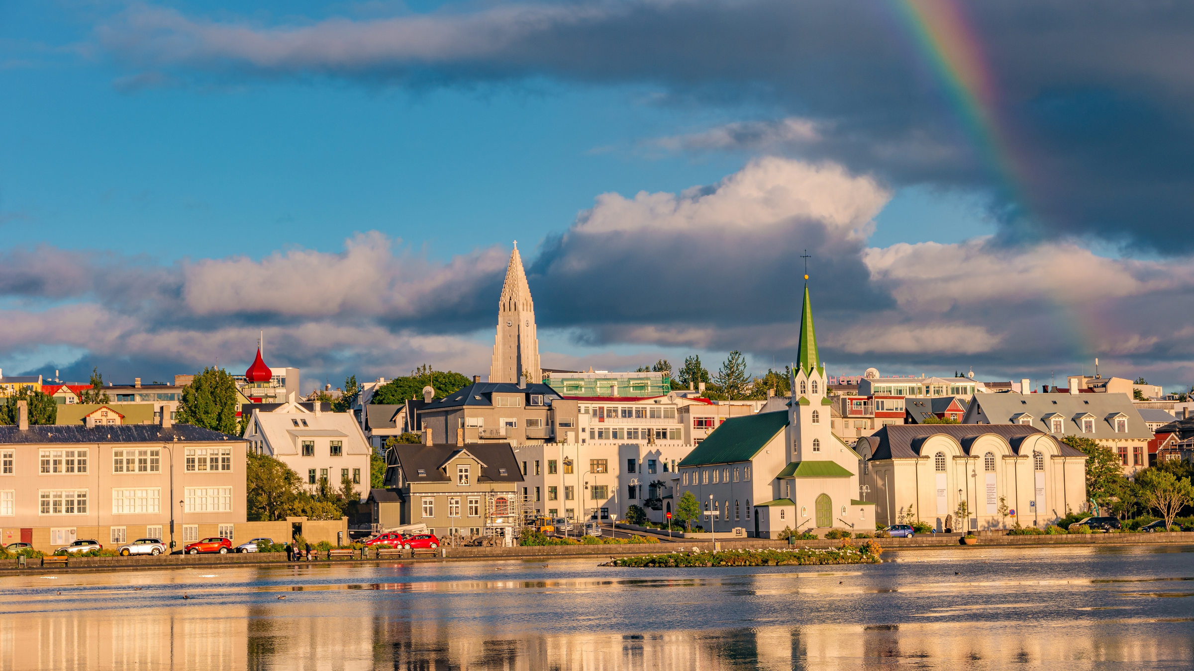 Historical and touristic downtown in Reykjavik at sunset and rainbow in Iceland. Cityscape at golden hour and blue sky at inner lake around Tjornin city park in the downtown.