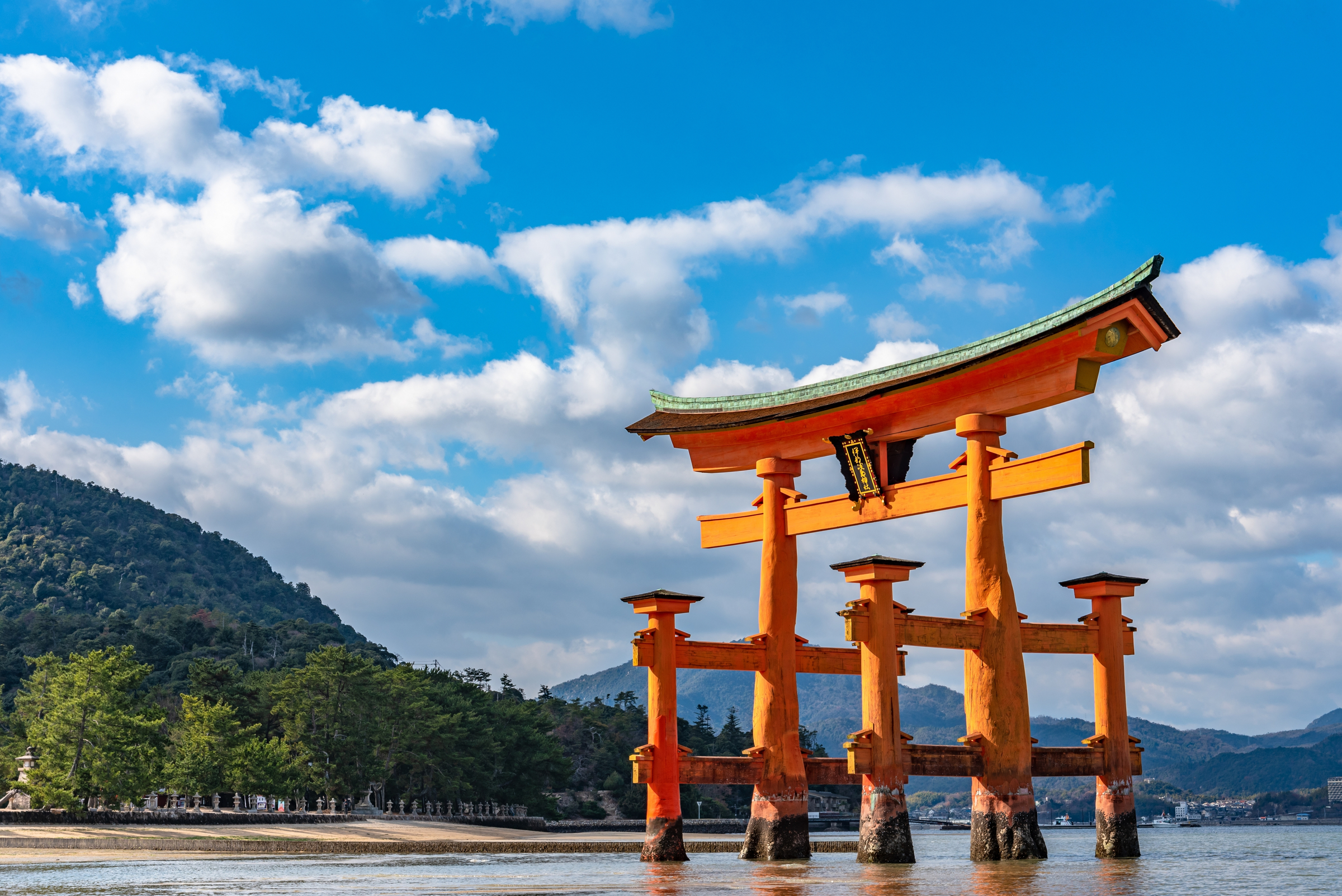 Close-up Floating orange red giant Grand O-Torii gate stands in Miyajima island bay beach at low tide on sunny day. Hiroshima City. The Three Views of Japan. Translation on gate : Itsukushima Shrine