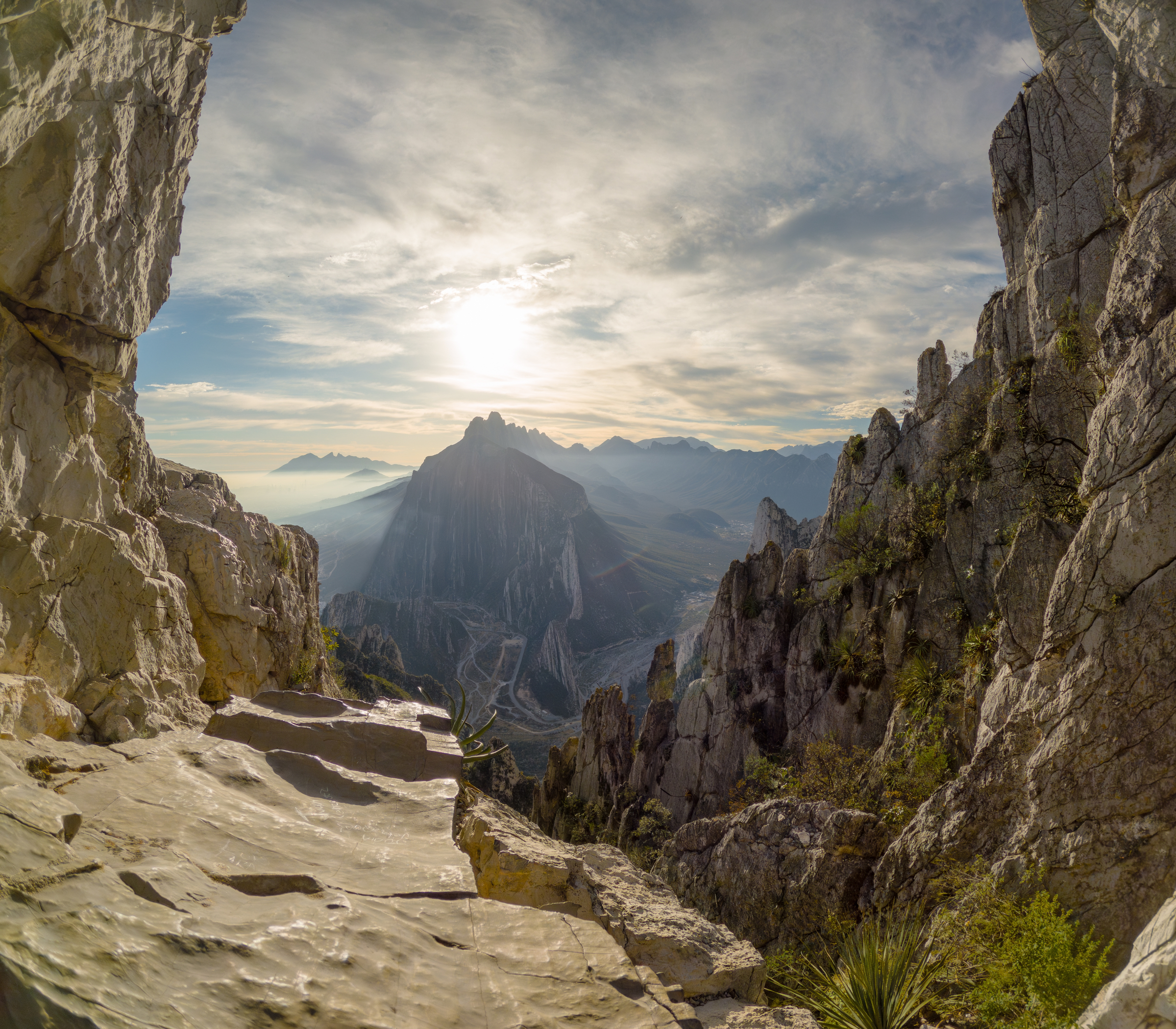 View of the rocky cliffs and mountainous landscape of Monterrey at sunrise, with the sun casting a golden glow over the rugged terrain. The distant peaks create a dramatic backdrop against the morning