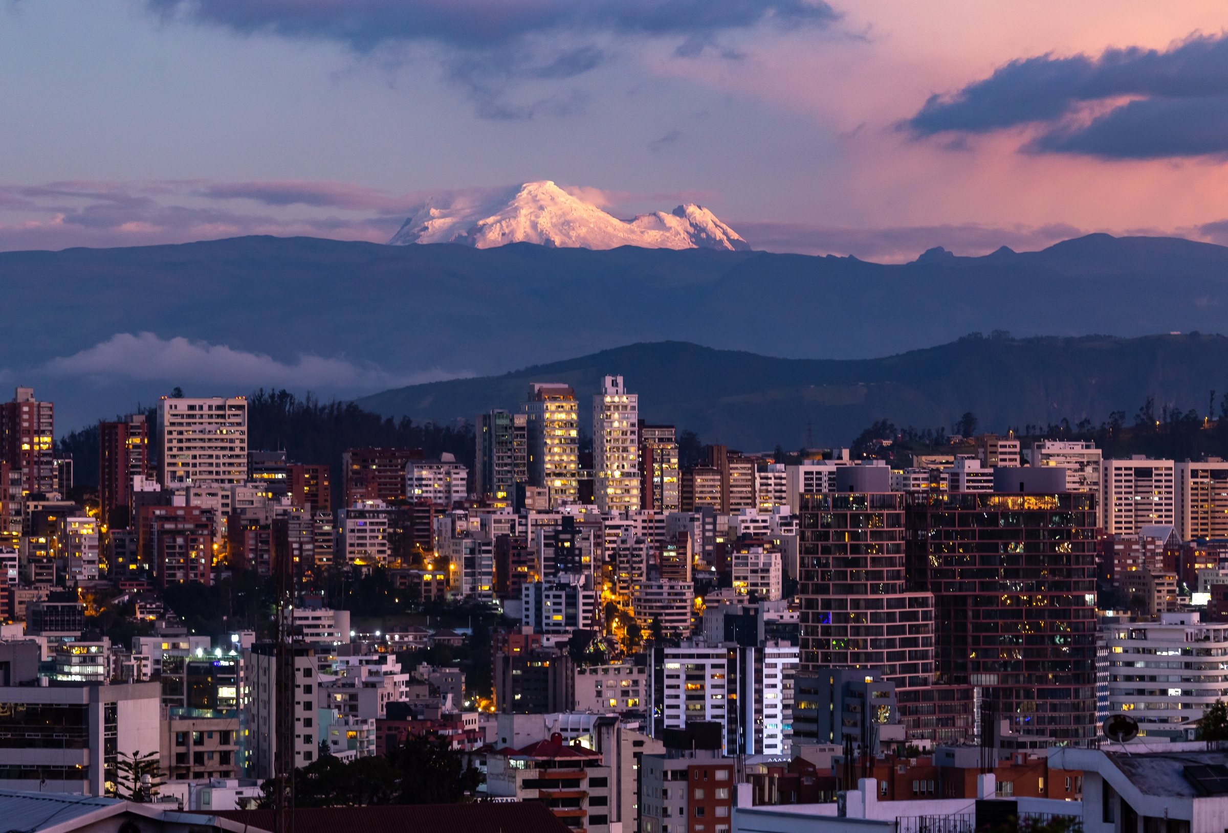 Quito buildings illuminated with the Antisana volcano in the background at dusk.