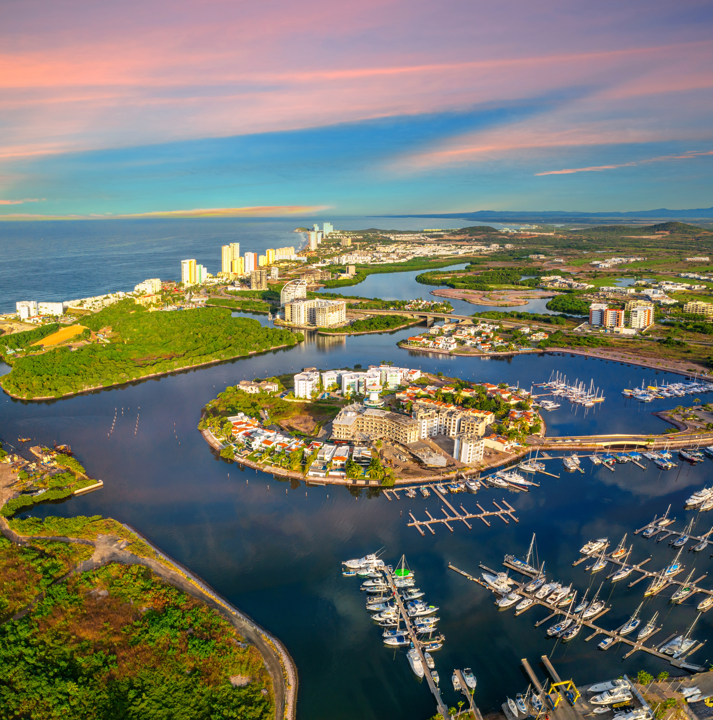 Panoramic view of the Mazatlán marina at sunrise, warm colors and a sky with clouds, view of boats on the lake and the sea in the background