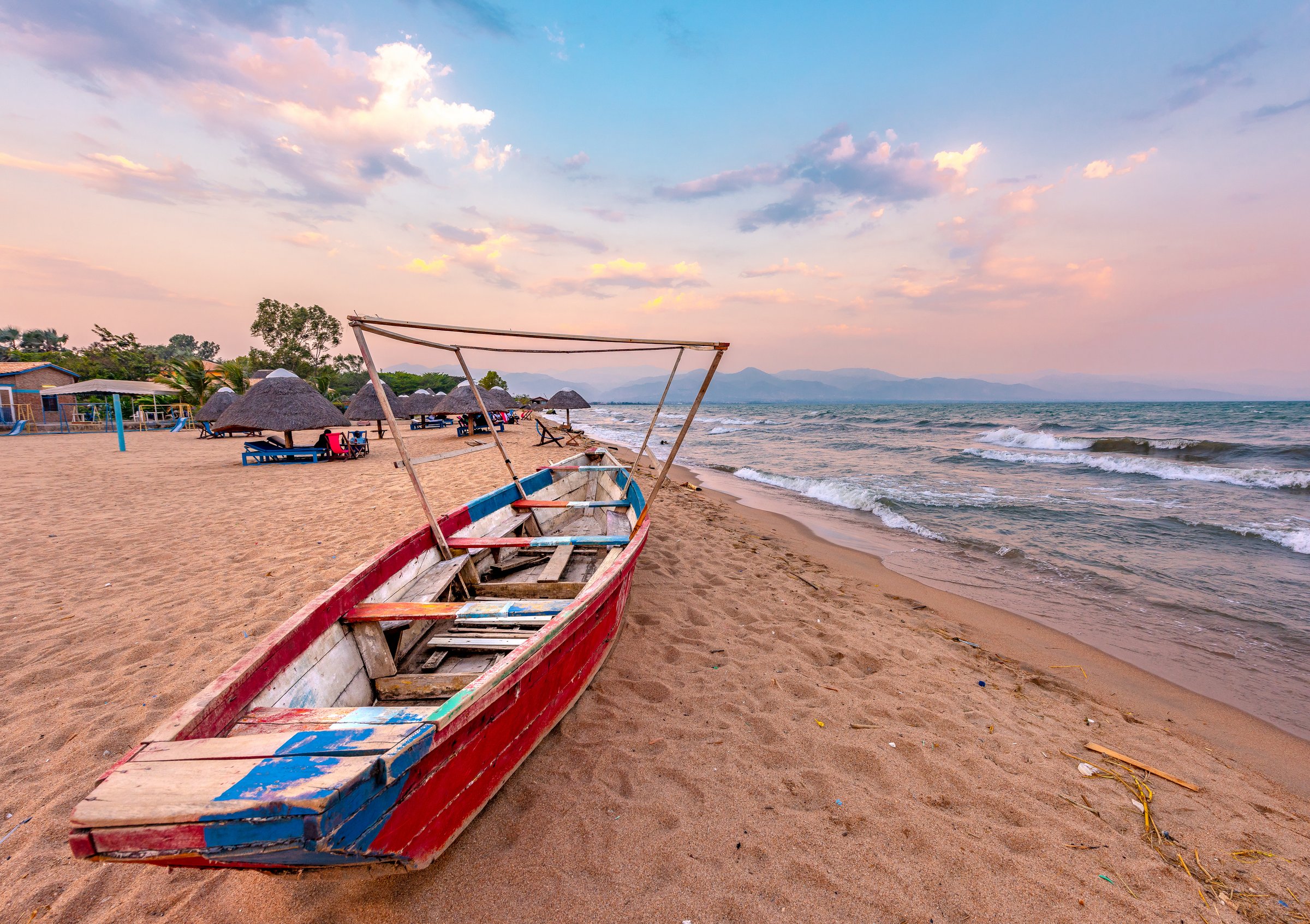 Burundi Bujumbura lake Tanganyika, windy cloudy sky and sand beach at sea lake in East Africa, Burundi sunset with boat from wood. Thatch african roofs on umbrellas