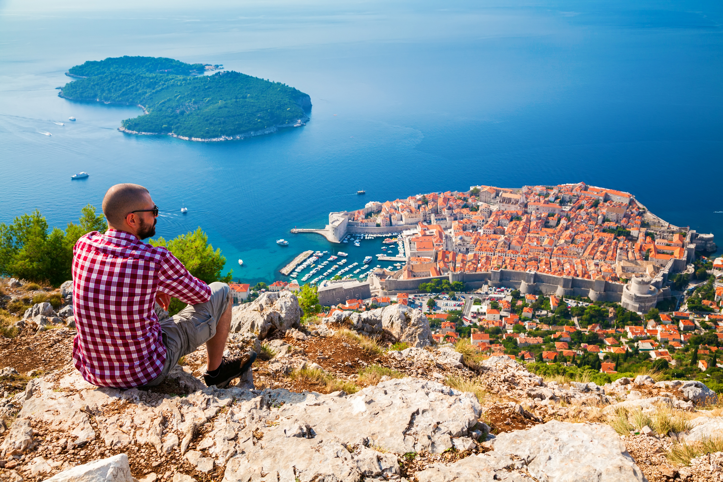 tourist man looking down to the Old Town of Dubrovnik, sitting on the mountain above the city, Croatia