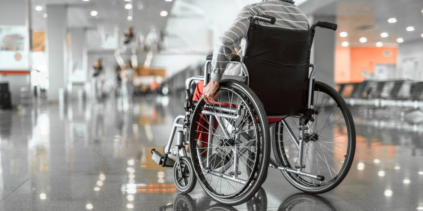 Back view photo of old woman moving in wheelchair in the lobby at airport. Copy space in left side