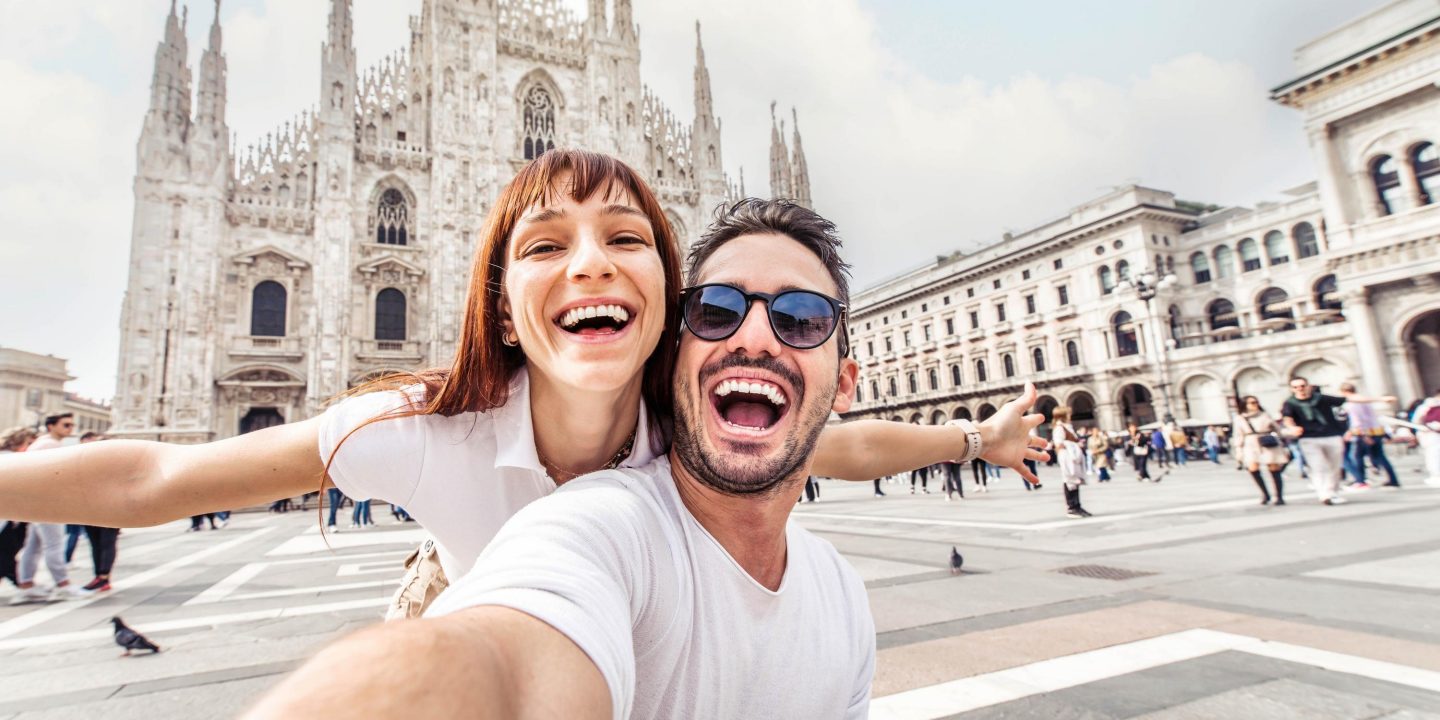 Happy couple taking selfie in front of Duomo cathedral in Milan, Lombardia - Two tourists having fun on romantic summer vacation in Italy - Holidays and traveling lifestyle concept