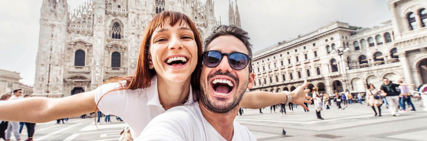 Happy couple taking selfie in front of Duomo cathedral in Milan, Lombardia - Two tourists having fun on romantic summer vacation in Italy - Holidays and traveling lifestyle concept