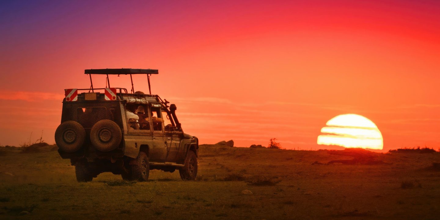 A safari vehicle with top up driving toward the rising sun on the horizon in Masai Mara, Kenya.