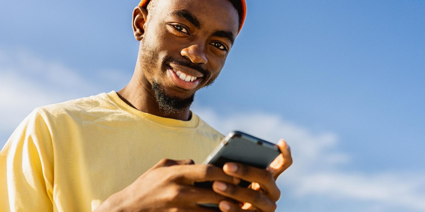 Stylish cool teen male skateboarder at skate park using smartphone