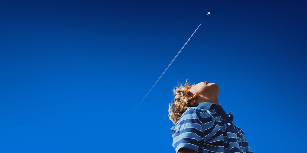 Un enfant blond regarde le ciel et observe un avion