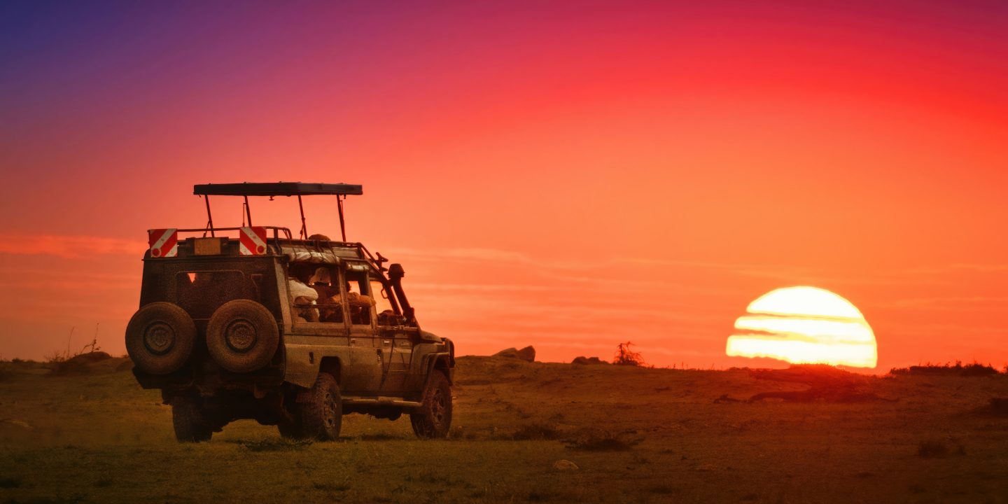 A safari vehicle with top up driving toward the rising sun on the horizon in Masai Mara, Kenya.